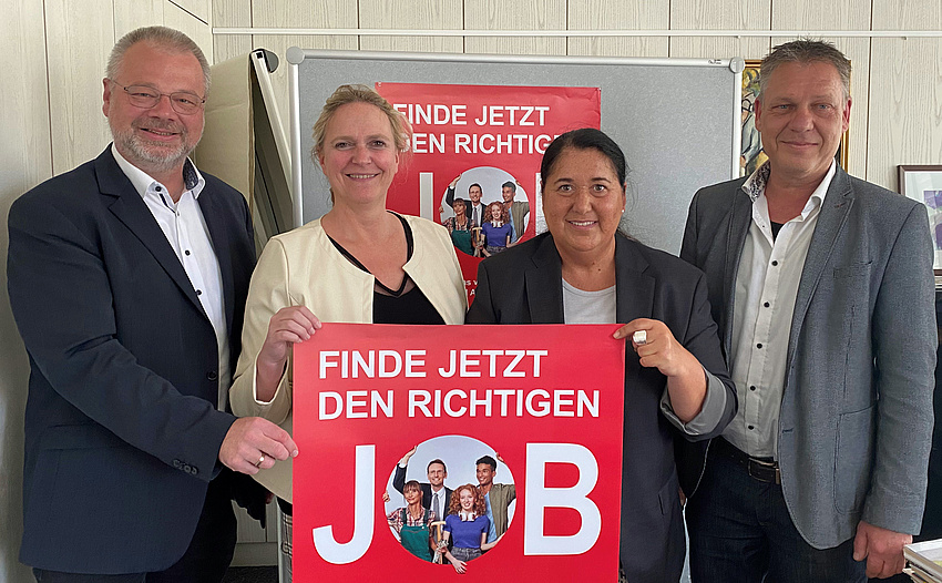 Zwei Männer und zwei Frauen stehen nebeneinander. Die beiden Frauen halten ein Plakat. Darauf steht: Finde jetzt den richtigen Job.