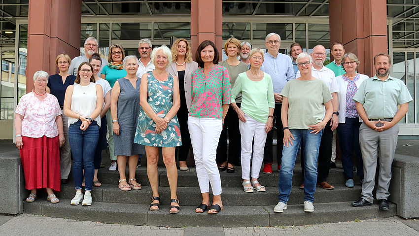 Eine Gruppe Männer und Frauen steht vor und auf den Treppen zu einem Gebäude