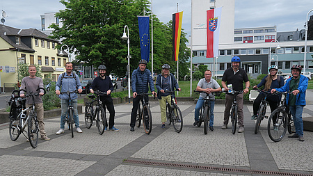 Mehrere Personen stehen mit ihren Fahrrädern auf einem größeren Platz nebeneinander.