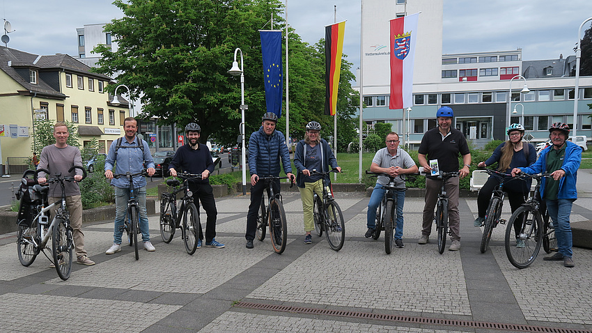 Mehrere Personen stehen mit ihren Fahrrädern auf einem größeren Platz nebeneinander.