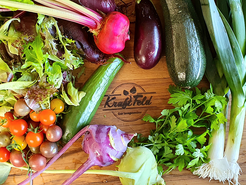 verschiedene bunte Gemüsearten wie Rote Beete und Zucchini auf einem Holzbrett mit dem Logo Kraftfeld Gartengemüse