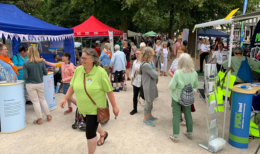 Eine Promenade, links und rechts sind Stände aufgebaut. Dazwischen laufen Menschen, die sich an den Ständen informieren.