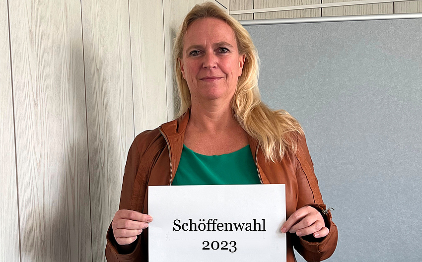 Eine Frau hält ein Blatt Papier in die Kamera. Auf dem Papier steht: Schöffenwahl 2023