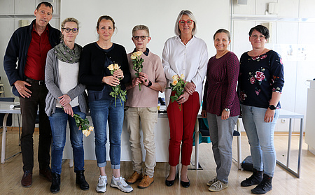 Ein Mann und sechs Frauen stehen nebeneinander und lächeln in die Kamera. Vier der Frauen haben Rosen in der Hand.