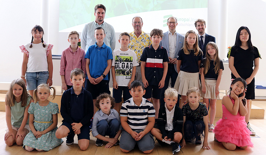 Kinder, Jugendliche und Erwachsene stehen zu einem Gruppenfoto in zwei Reihen hintereinander. Die Kinder vorne in der Hocke.