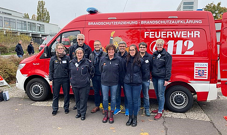 Eine Personengruppe steht vor einem Kleinbus der Feuerwehr.