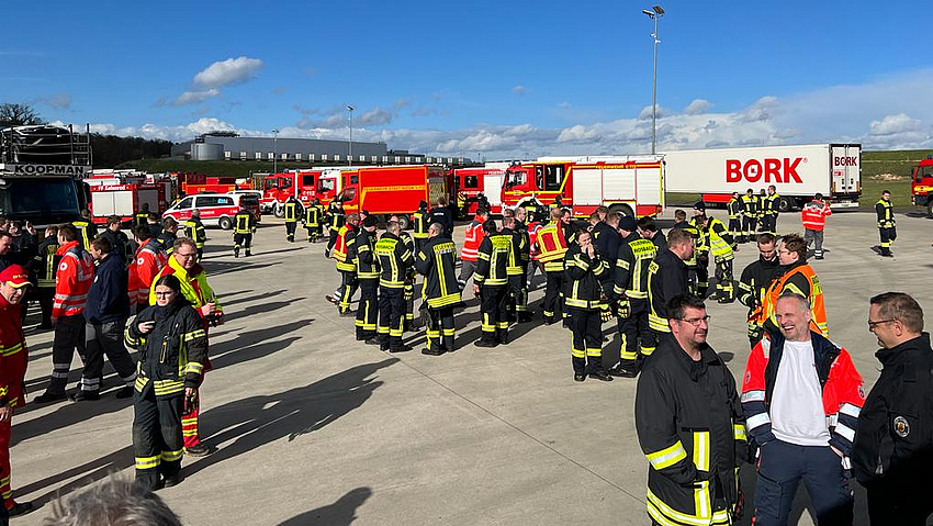 Einsatzkräfte in Uniform und Feuerwehrfahrzeuge auf einem großen Platz im Freien.