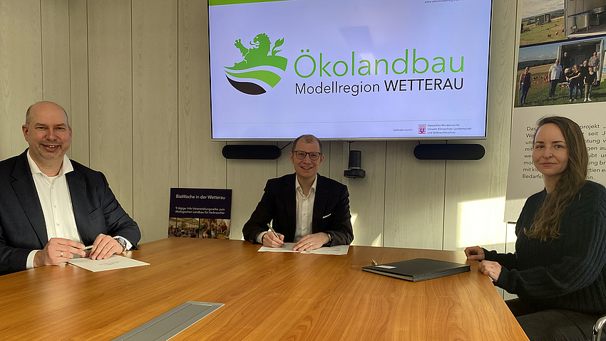 Drei Personen an einem Konferenztisch. Im Hintergrund ein Flachbildschirm mit einer Präsentation zum Ökolandbau.