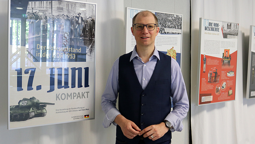 Landrat Jan Weckler vor den Bilderrahmen mit den Plakaten der Ausstellung