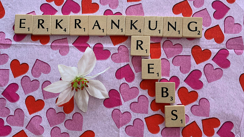 Auf einer Serviette liegen kleine Holzklötzchen, auf denen Buchstaben aufgedruckt sind. Sie ergeben die Worte Erkrankung und Krebs.