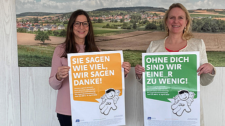 Zwei Frauen halten jweils ein Plakat in der Hand.