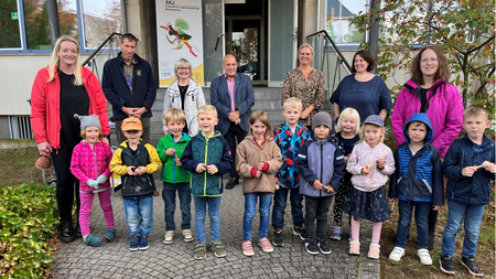 Eine Gruppe Kindergartenkinder. Dahinter mehrere Erwachsene. Im Hintergrund ein Hauseingang.