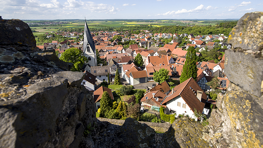 Blick auf Häuser und eine Kirche. Im Vordergrund eine felsige Burgmauer.