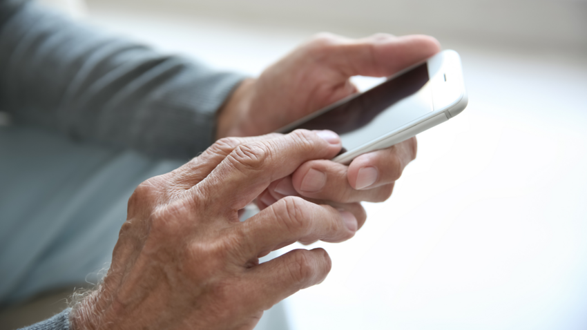 Ein älterer Mann hält ein Mobiltelefon in der Hand.