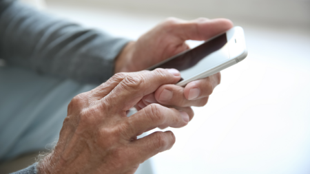 Ein älterer Mann hält ein Mobiltelefon in der Hand.