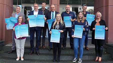 Eine Personengruppe steht auf der Treppe zum Kreishaus. Sie lächeln in die Kamera und haben Urkunden in der Hand.