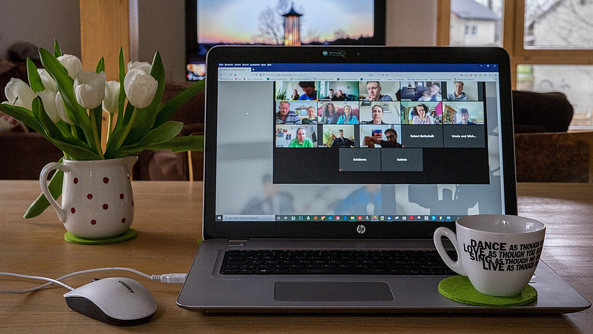 Ein aufgeklappter Laptop. Daneben eine Vase mit Blumen und eine Kaffeetasse.