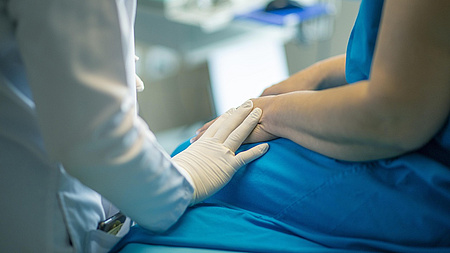 Zu sehen ist die Hand eines Arztes oder einer Ärztin. Die Person trägt Handschuhe und kümmert sich um einen Patienten.