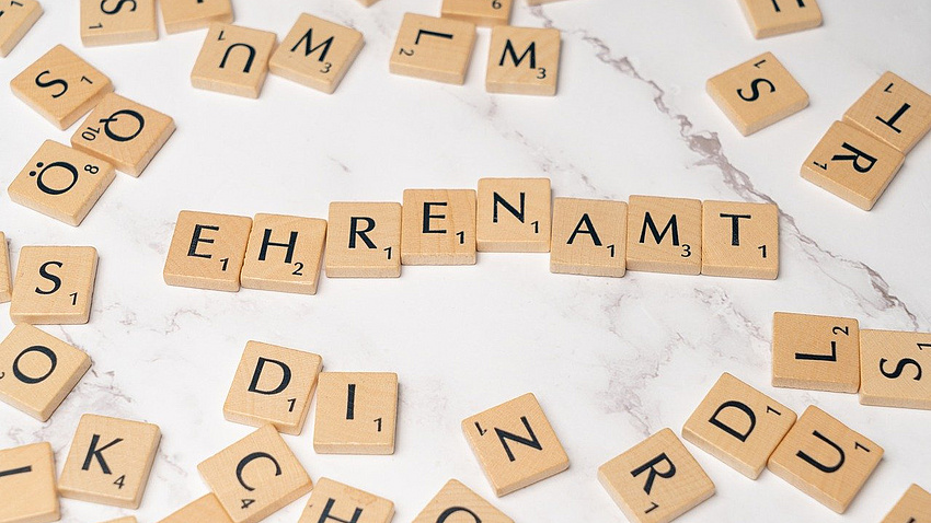 Zu sehen ist ein Symbolfoto. Scrabblesteine bilden das Wort "Ehrenamt".