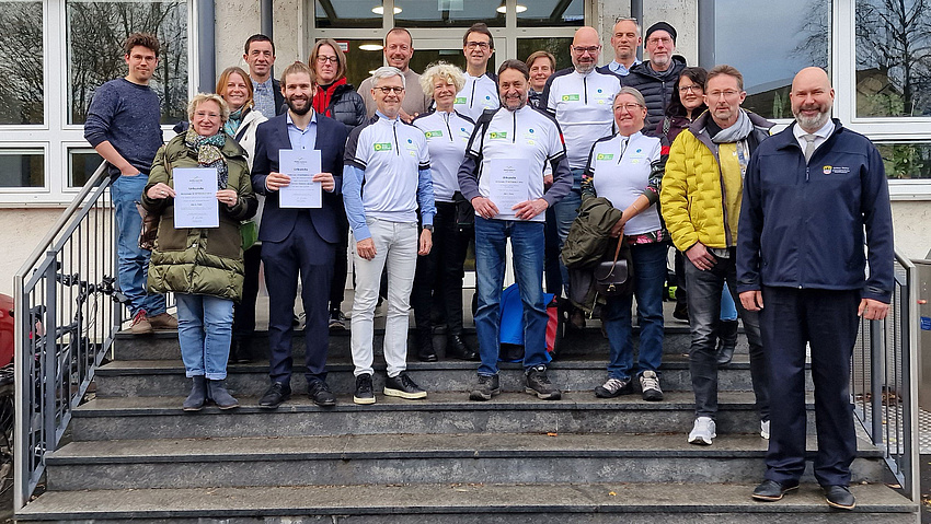 Eine Gruppe von rund 20 Personen steht auf einer Treppe. Sie halten Urkunden in die Höhe und tragen Fahrradtrikots.