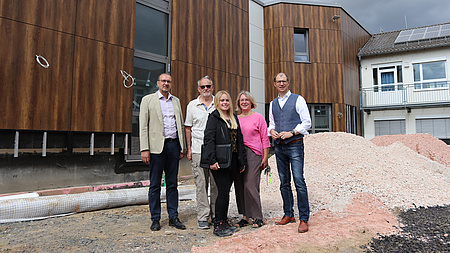 Fünf Menschen stehen auf einer Baustelle vor einem Neubau.