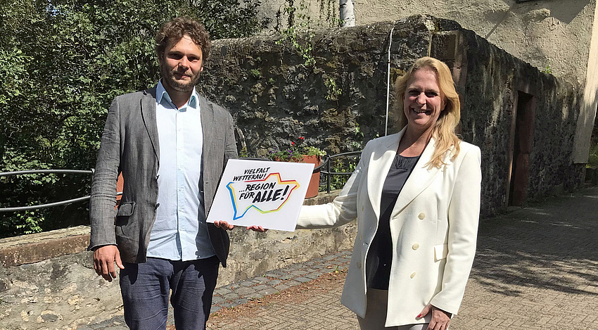 Ein Mann und eine Frau halten geimnesam das Label mit dem Aufdruck Vielfalt Wetterau in der Hand. Im Hintergrund ein altes Gebäude