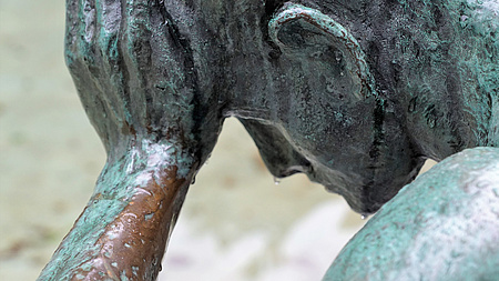 Metallskulptur von der Seite. Eine Person stützt mit einer traurigen Geste den Kopf mit der linken Hand.