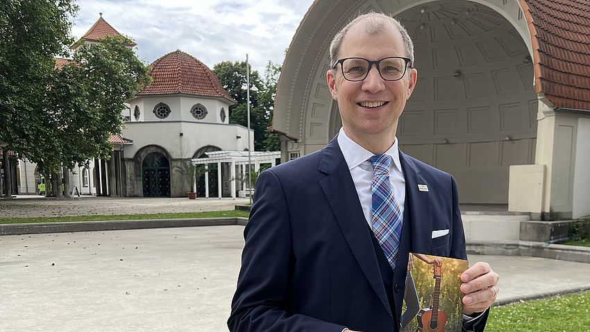 Ein man steht in einem Park und hält ein Prospekt in die Kamera.