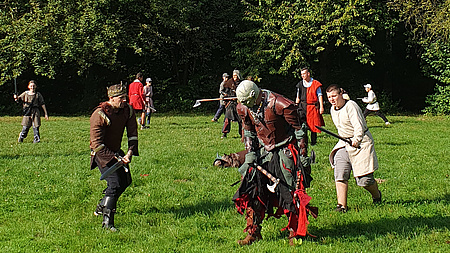 Mehrere Menschen auf einer großen Wiese in verschiedenen Verkleidungen. Im Vordergrund sind ein Ork und ein König.