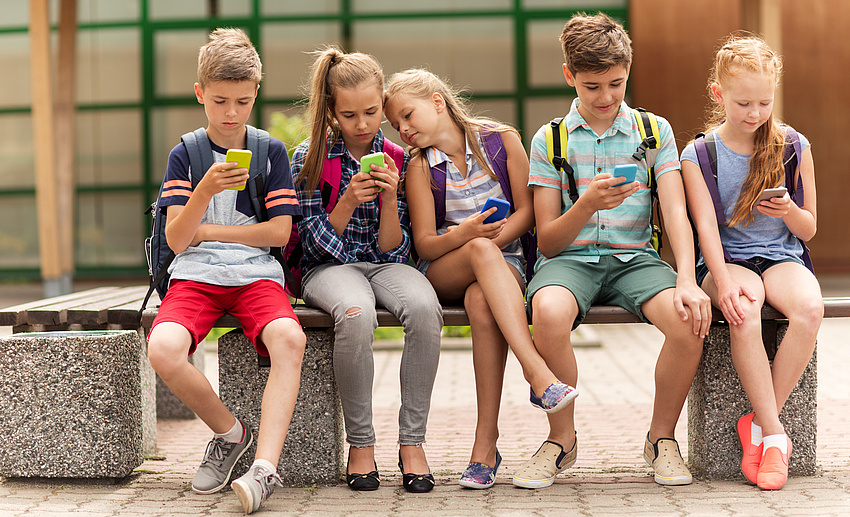 Jugendliche sitzend auf einer Mauer. Alle schauen auf ihr Handy.