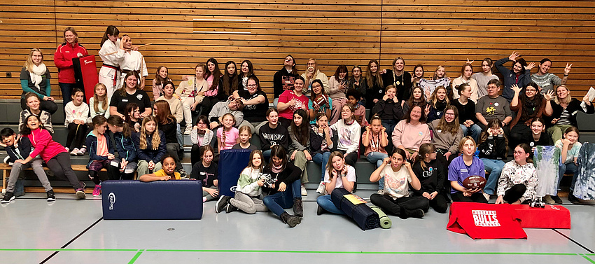 Eine große Gruppe Mädchen, junger und erwachsener Frauen in einer Turnhalle.