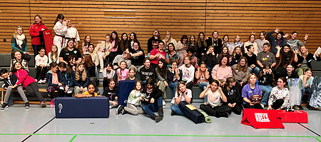 Eine große Gruppe Mädchen, junger und erwachsener Frauen in einer Turnhalle.