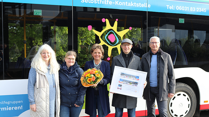 Drei Frauen und zwei Männer stehen vor einem beklebten Linienbus.